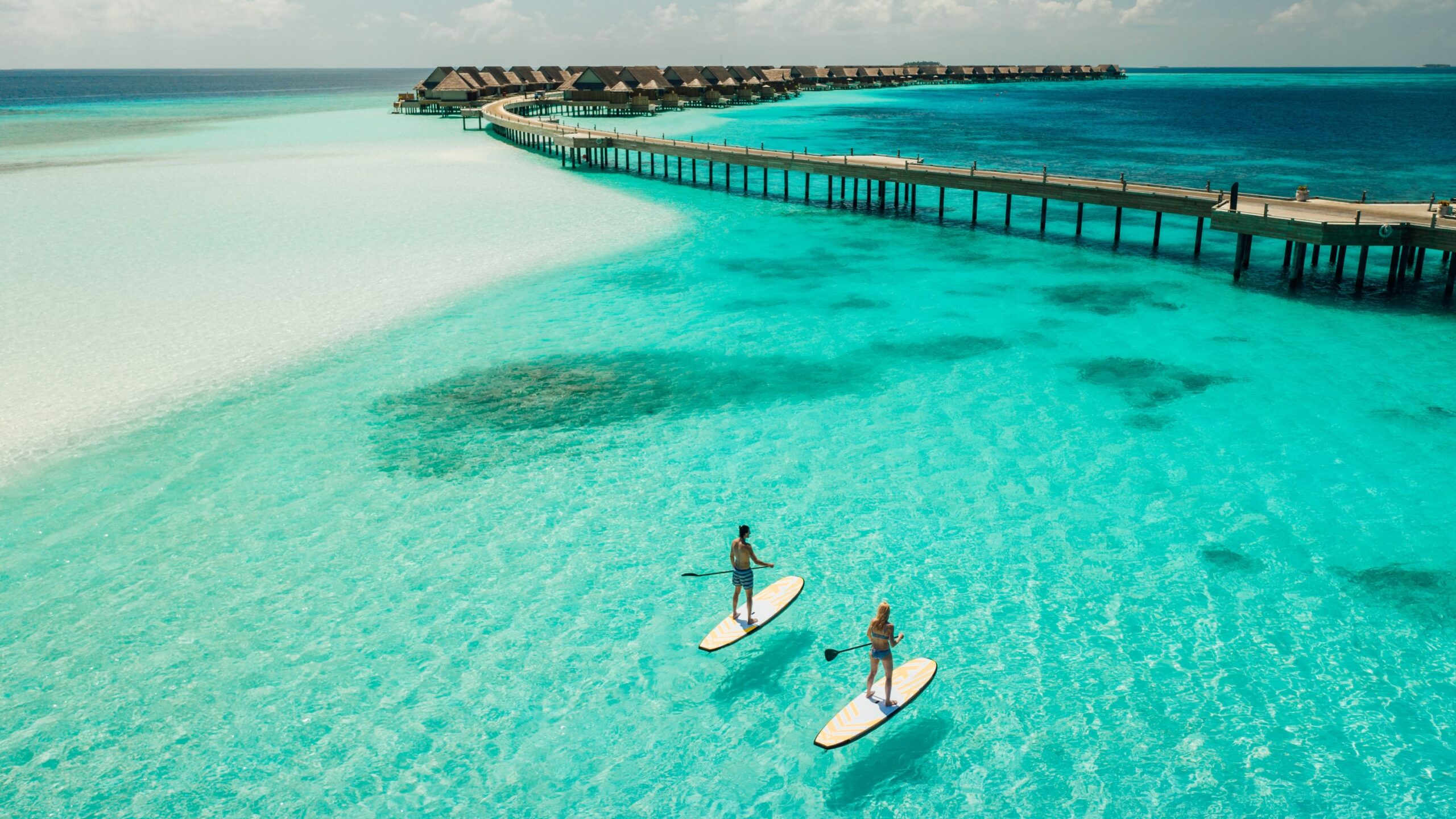 Maldives ocean shot from above with two travels on paddle board.